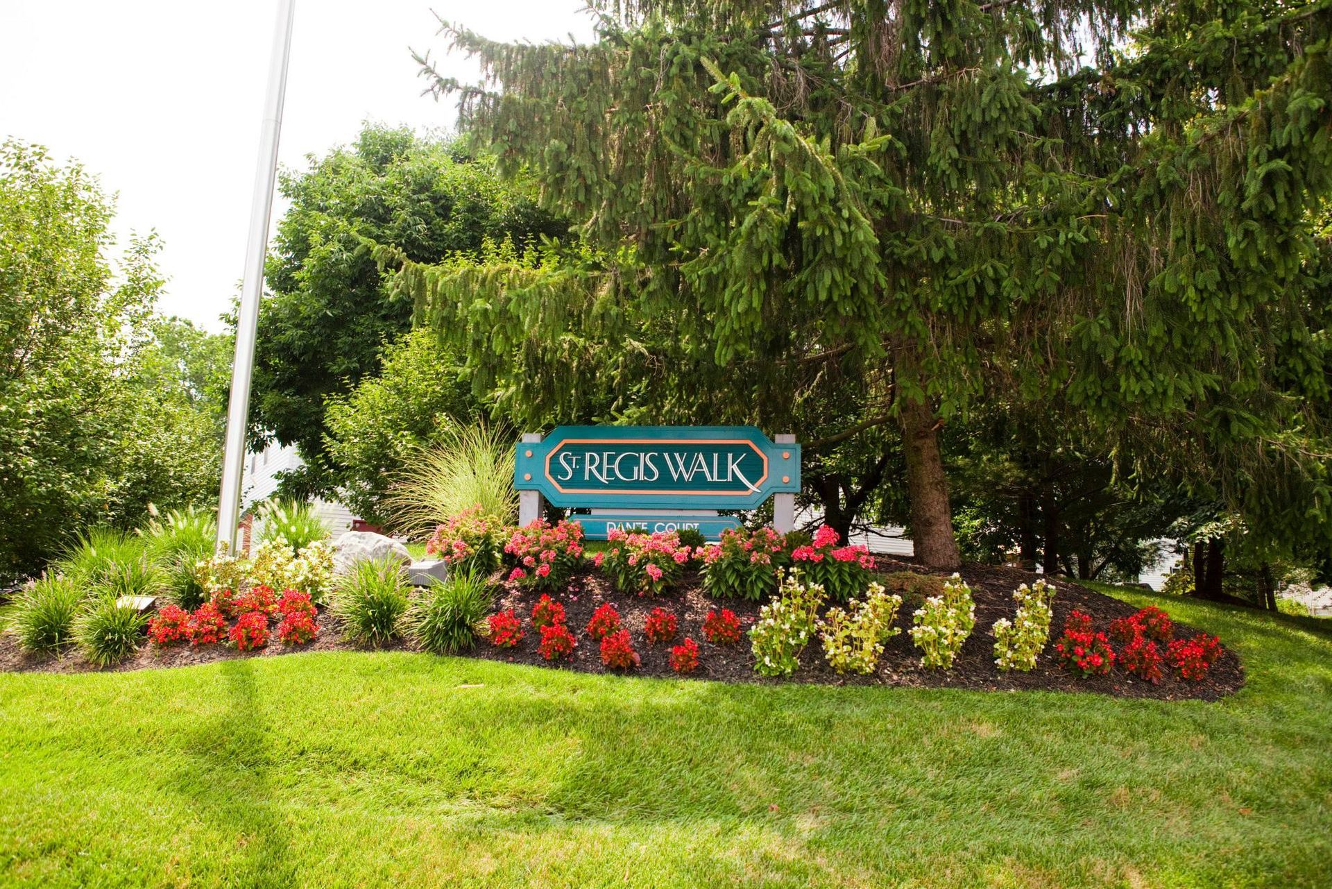 A sign in the middle of a lush green field surrounded by trees and flowers.