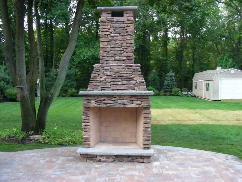 A stone fireplace in a backyard with a garage in the background