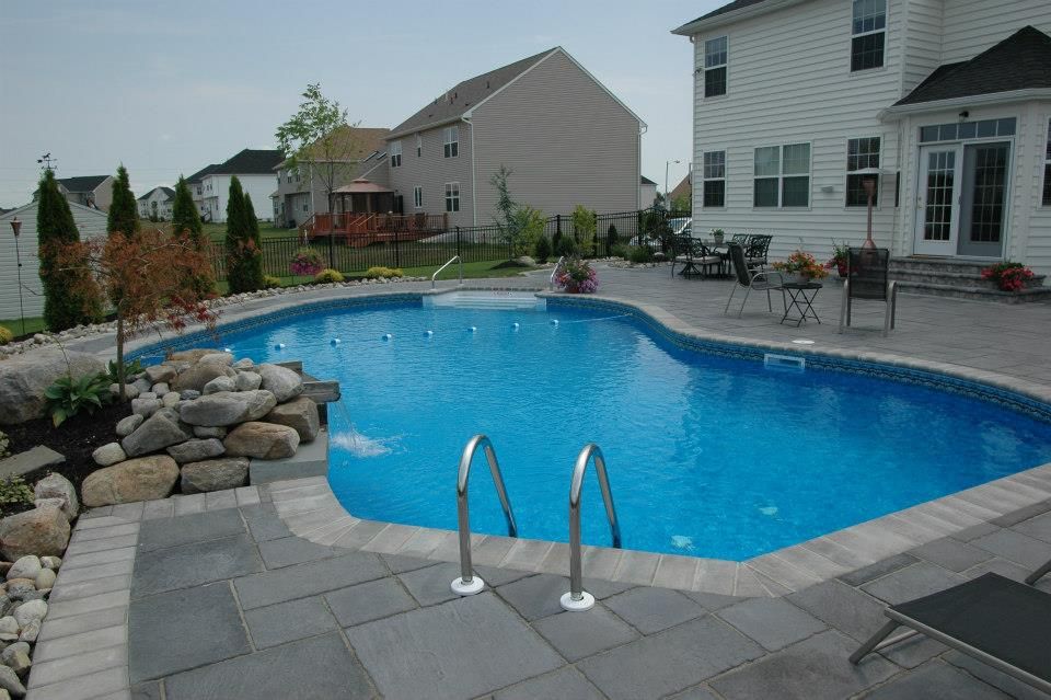 A large swimming pool with stairs leading to it in front of a house