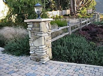 A stone pillar with a lamp on top of it next to a wooden fence.