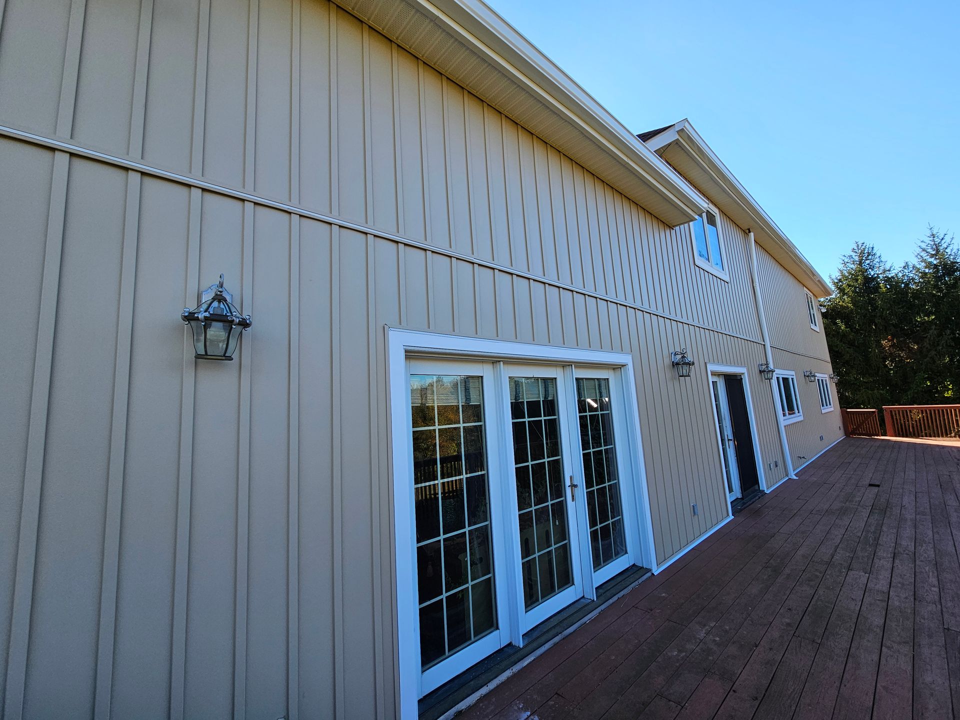 Beige building with white-framed glass doors and windows, brown deck, and blue sky.