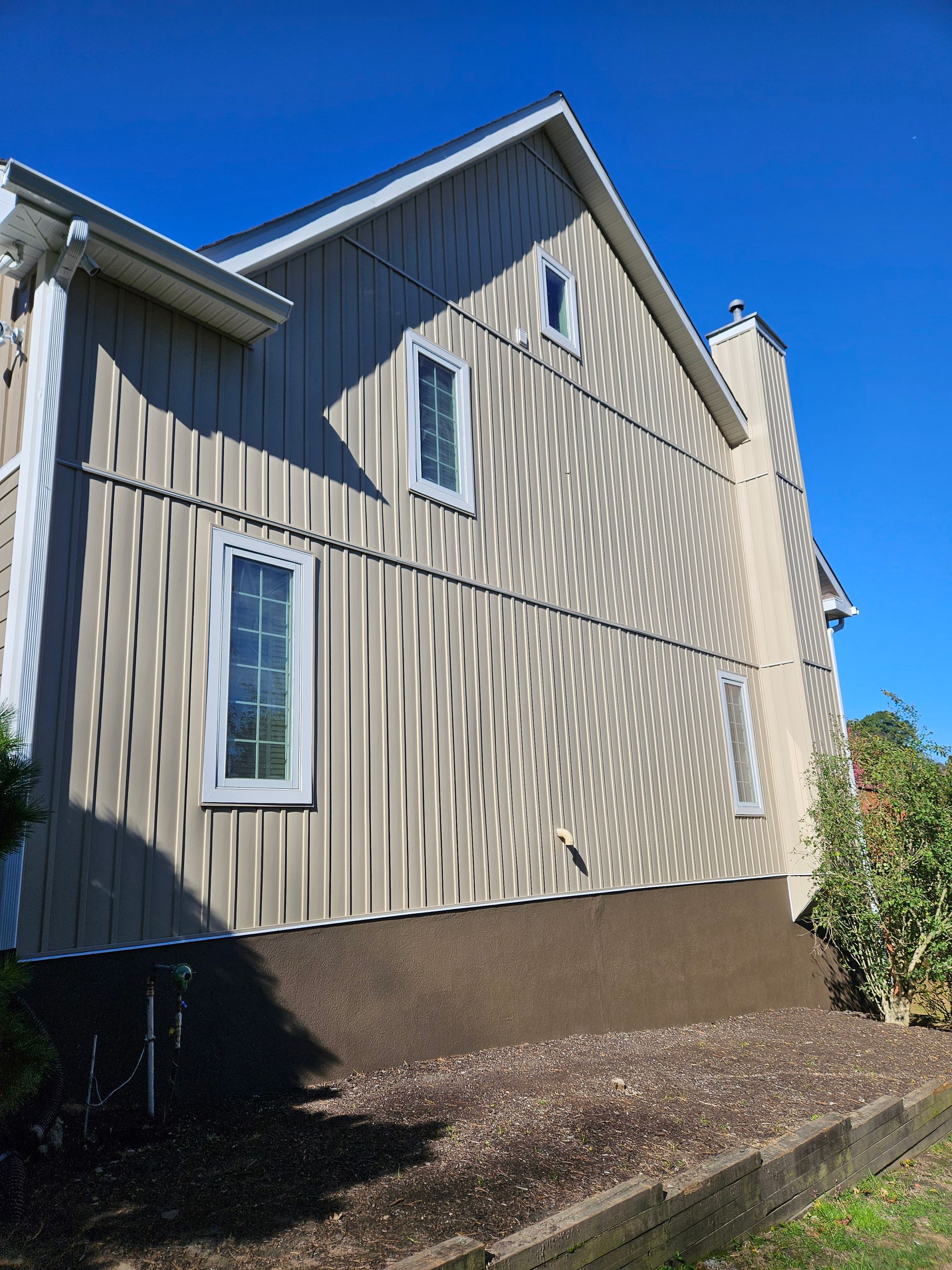 Beige house exterior with white trim, windows, and chimney, against a blue sky.