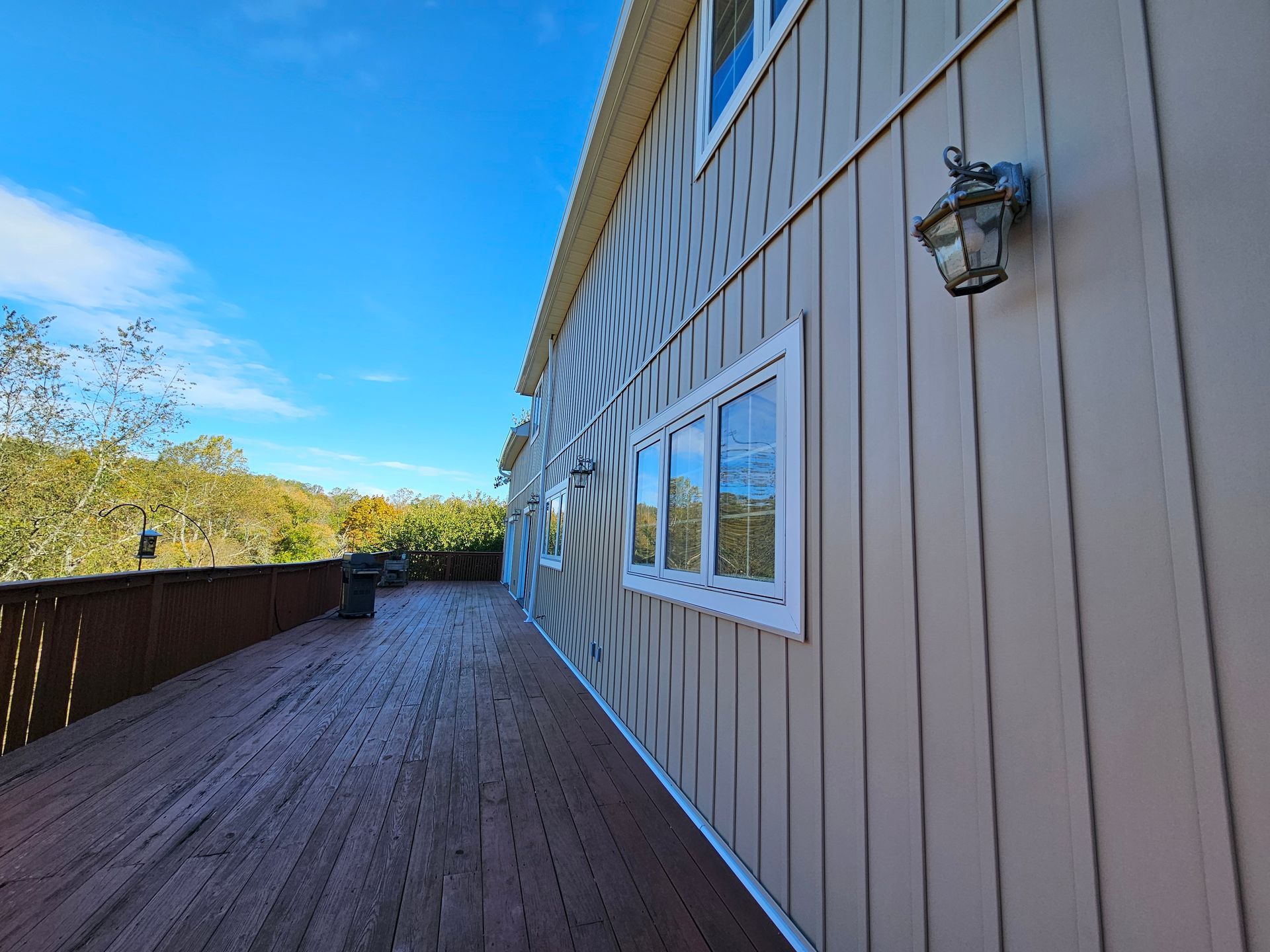 Wooden deck next to beige house with white-framed windows, against a bright blue sky.
