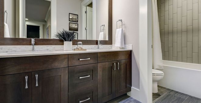 Modern bathroom with dark wood vanity, large mirror, and toilet beside a shower curtain.