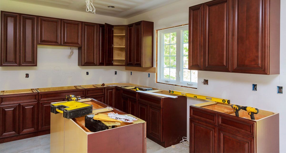 Unfinished kitchen with dark wood cabinets, beige walls, and yellow tools on countertops around a central island.