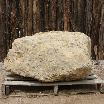 Large beige rock on a wooden pallet, against a backdrop of wooden poles.
