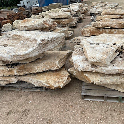 Stacks of large, light-colored flat stones on wooden pallets outdoors, presumably at a landscape supply yard.