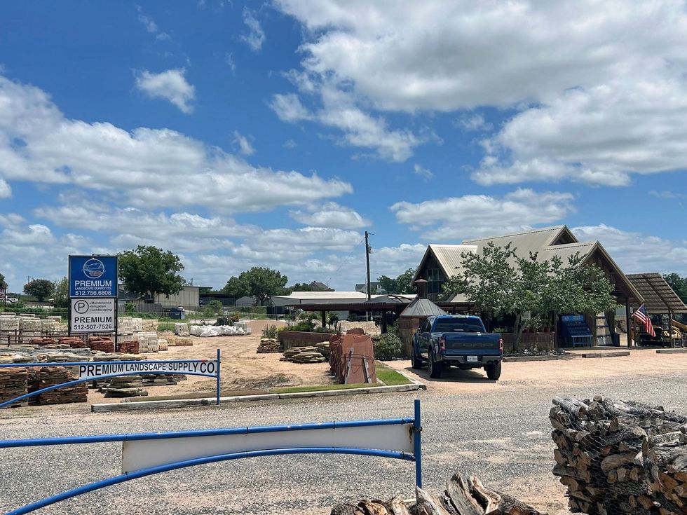 A sunny outdoor scene with a stone yard, a building with a rustic roof, and a blue truck.