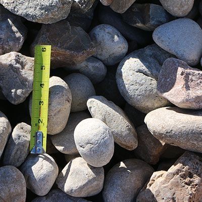 Rounded gray and tan river rocks with a yellow tape measure for scale.