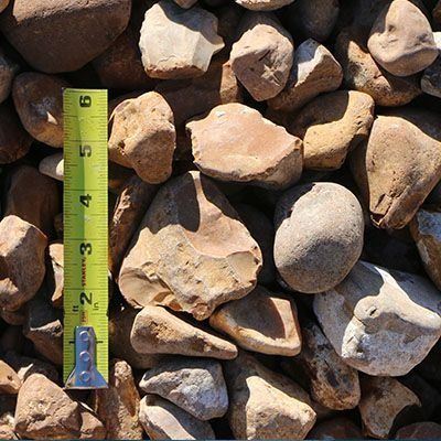 Tan and brown landscaping river rocks with a measuring tape for scale.