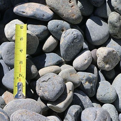 Pile of gray and blue river rocks with a yellow tape measure showing size.