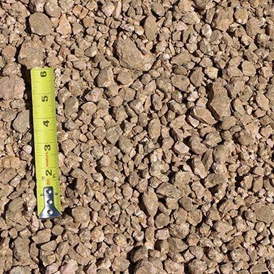 Gravel with a yellow tape measure for scale. Beige and brown rocks of various sizes.