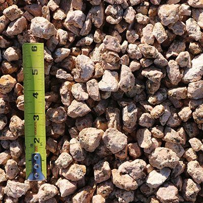 Tan gravel stones, shown close up with a yellow tape measure, are used for construction or landscaping.