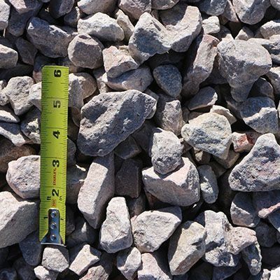 Gray gravel rocks with a yellow measuring tape, in an outdoor setting.