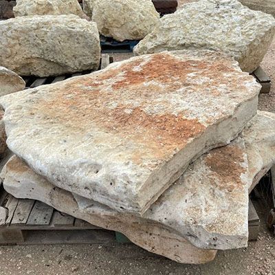 Stack of large, flat, beige and brown rocks on a wooden pallet, outdoors.