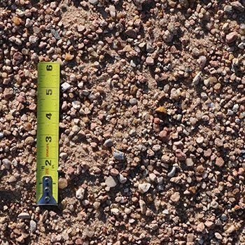 Brown gravel with small stones, sand, and a yellow tape measure for scale.
