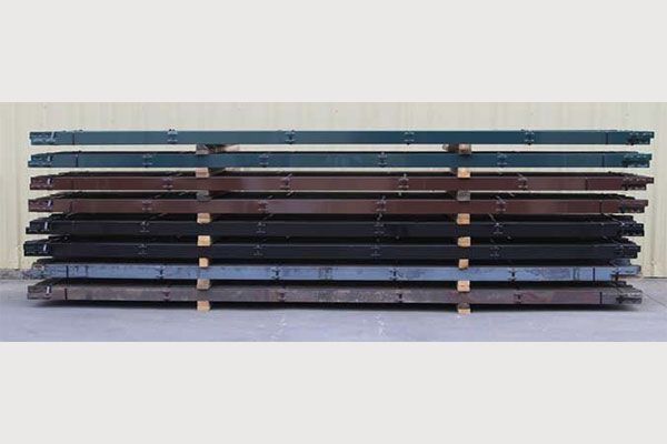 Rows of long, metal beams in varying dark colors, stacked on a wooden pallet.