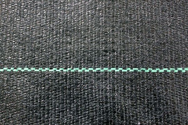Black woven landscape fabric with a green grid line running horizontally.