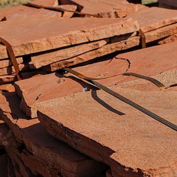 Stack of reddish-brown sandstone pavers, bundled with straps. Outdoors, close-up shot.