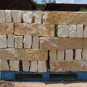 Pallet of rectangular beige and tan stone blocks wrapped in wire mesh.