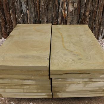 Stack of rectangular sandstone paving slabs, beige with swirling patterns, against a wood background.