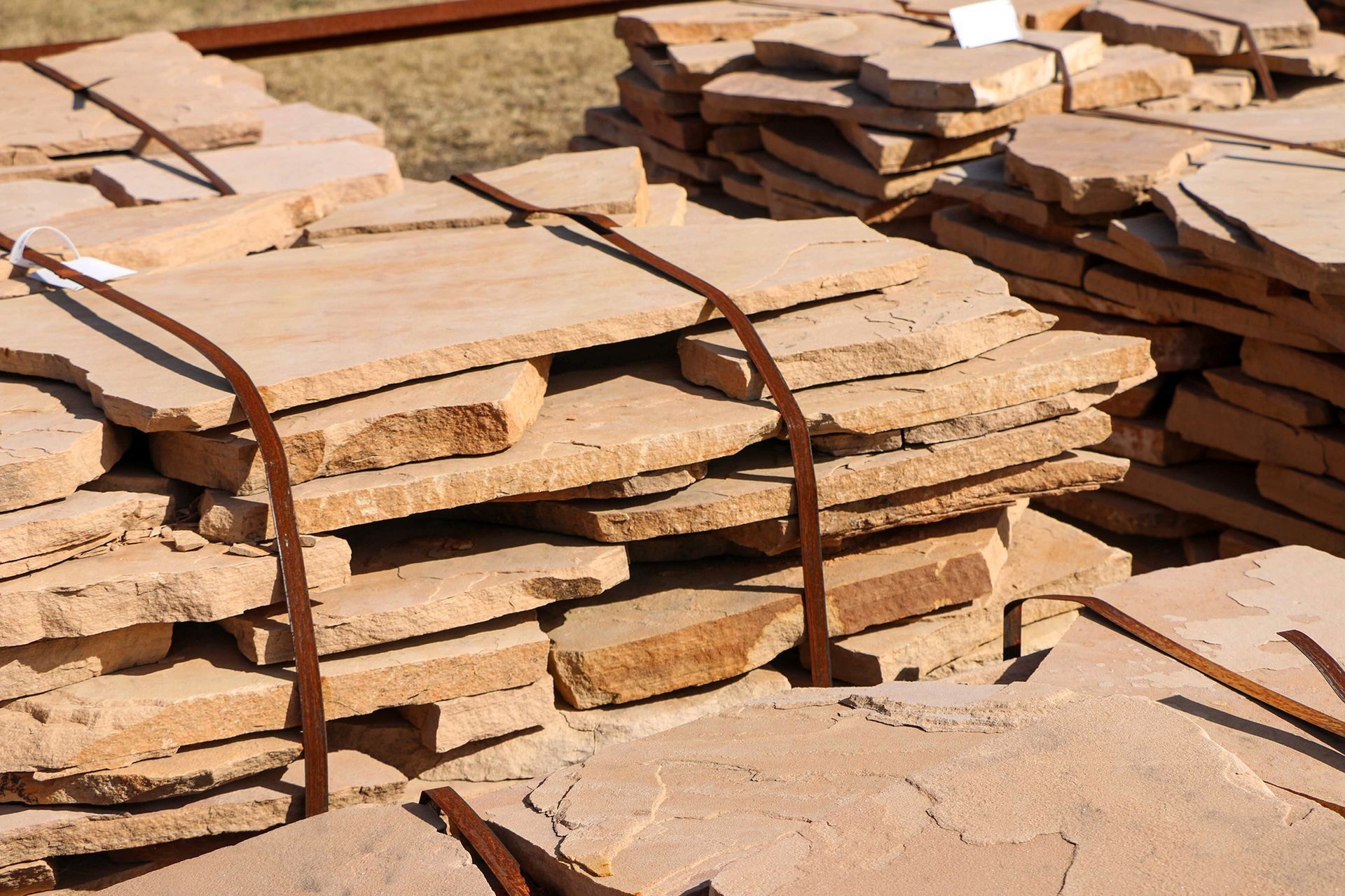 Stacks of rough-edged, tan-colored paving stones bundled with metal straps, outdoors.