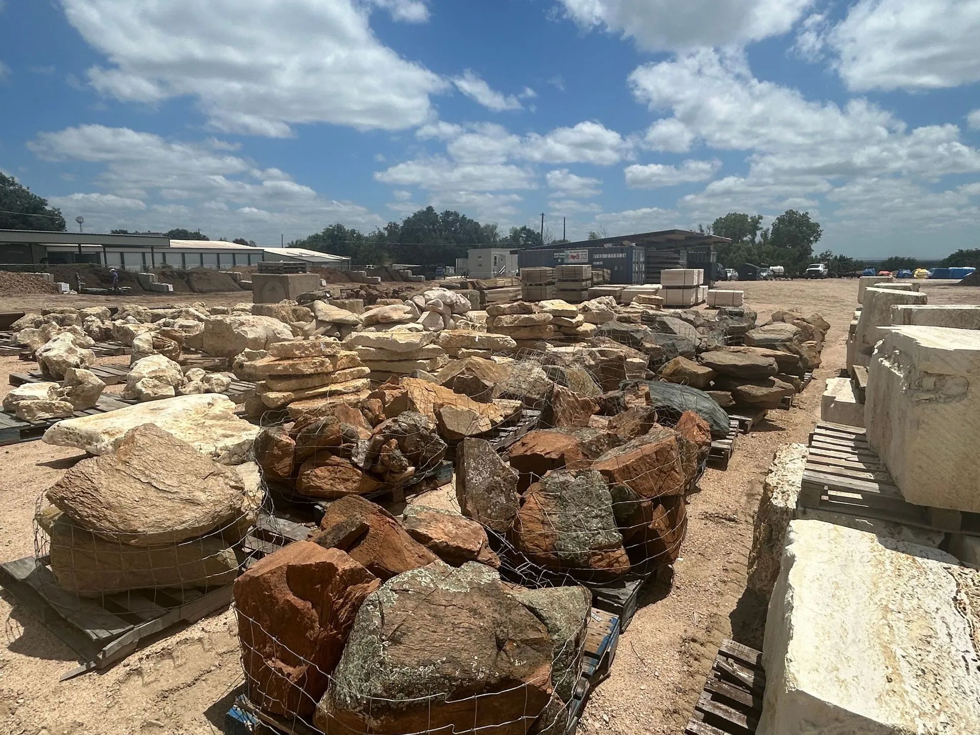 Rocks and stone blocks in a yard under a cloudy blue sky.