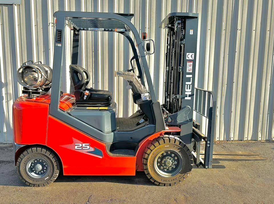 Red and gray forklift truck with propane tank parked in front of a corrugated wall.