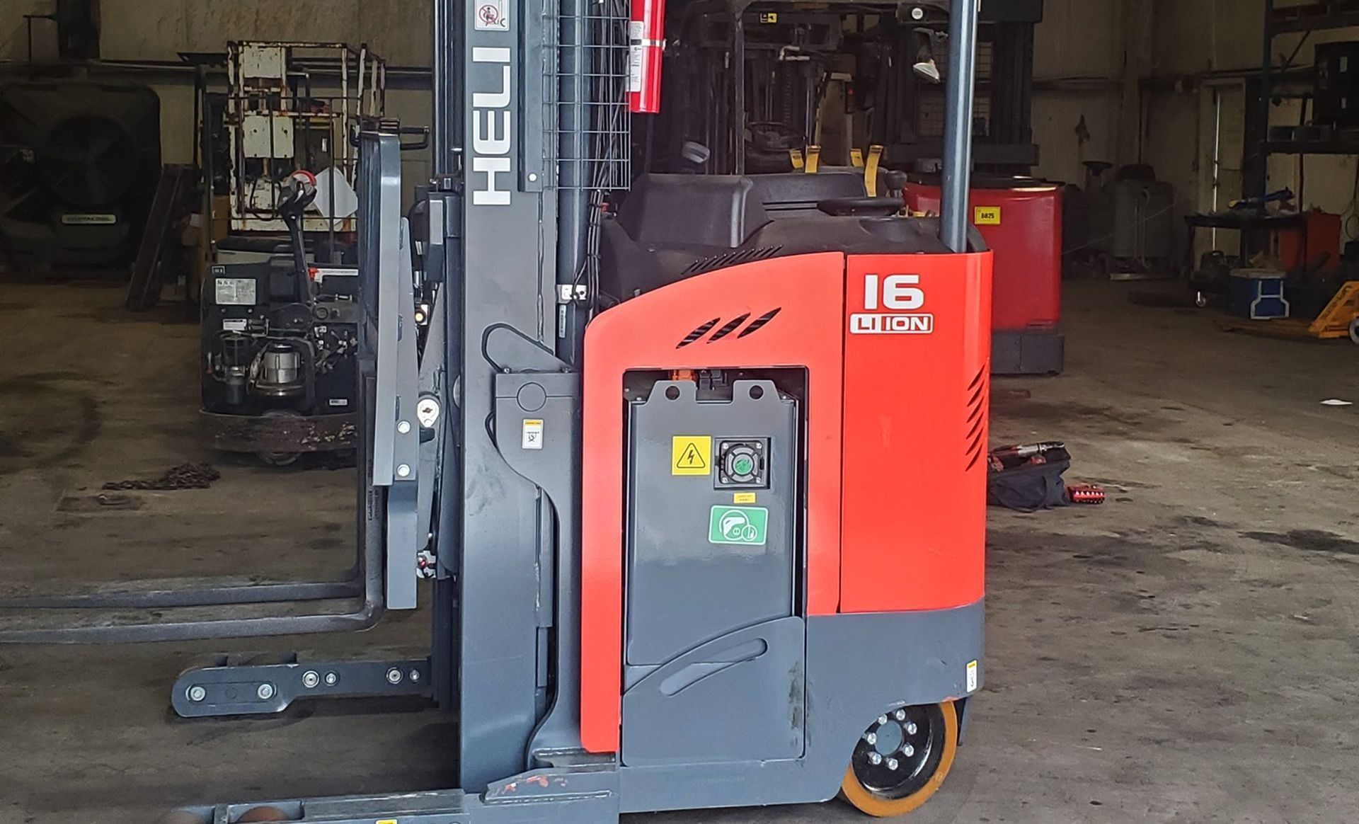 Red and gray stand-up forklift in a warehouse.