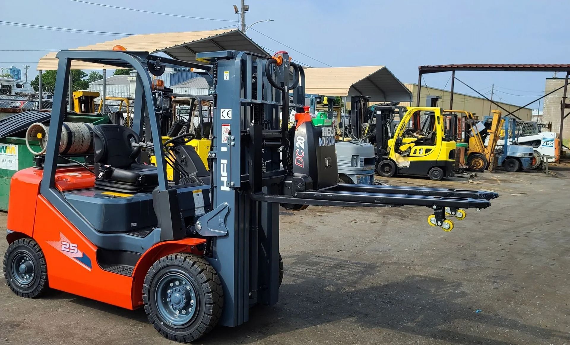 Orange and gray forklift with extended forks; other forklifts in a yard.