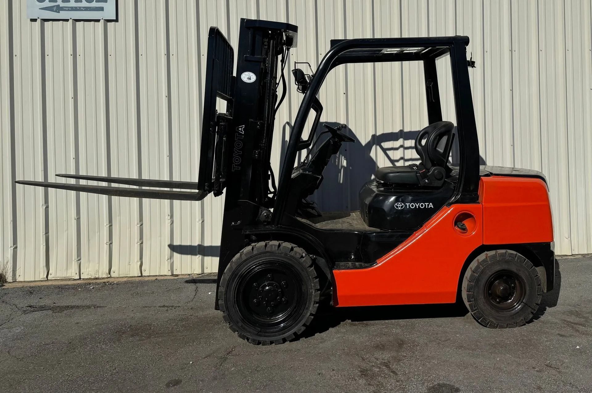 Orange and black Toyota forklift on pavement in front of a white building.