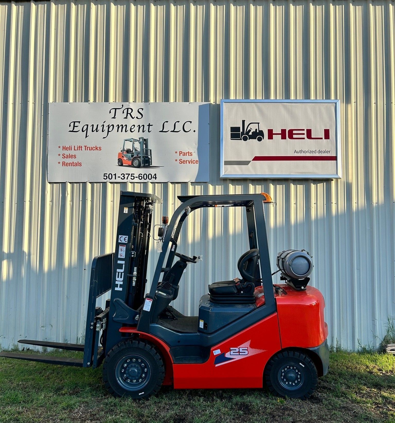 Red and gray HELI forklift parked in front of a sign for TRS Equipment LLC.