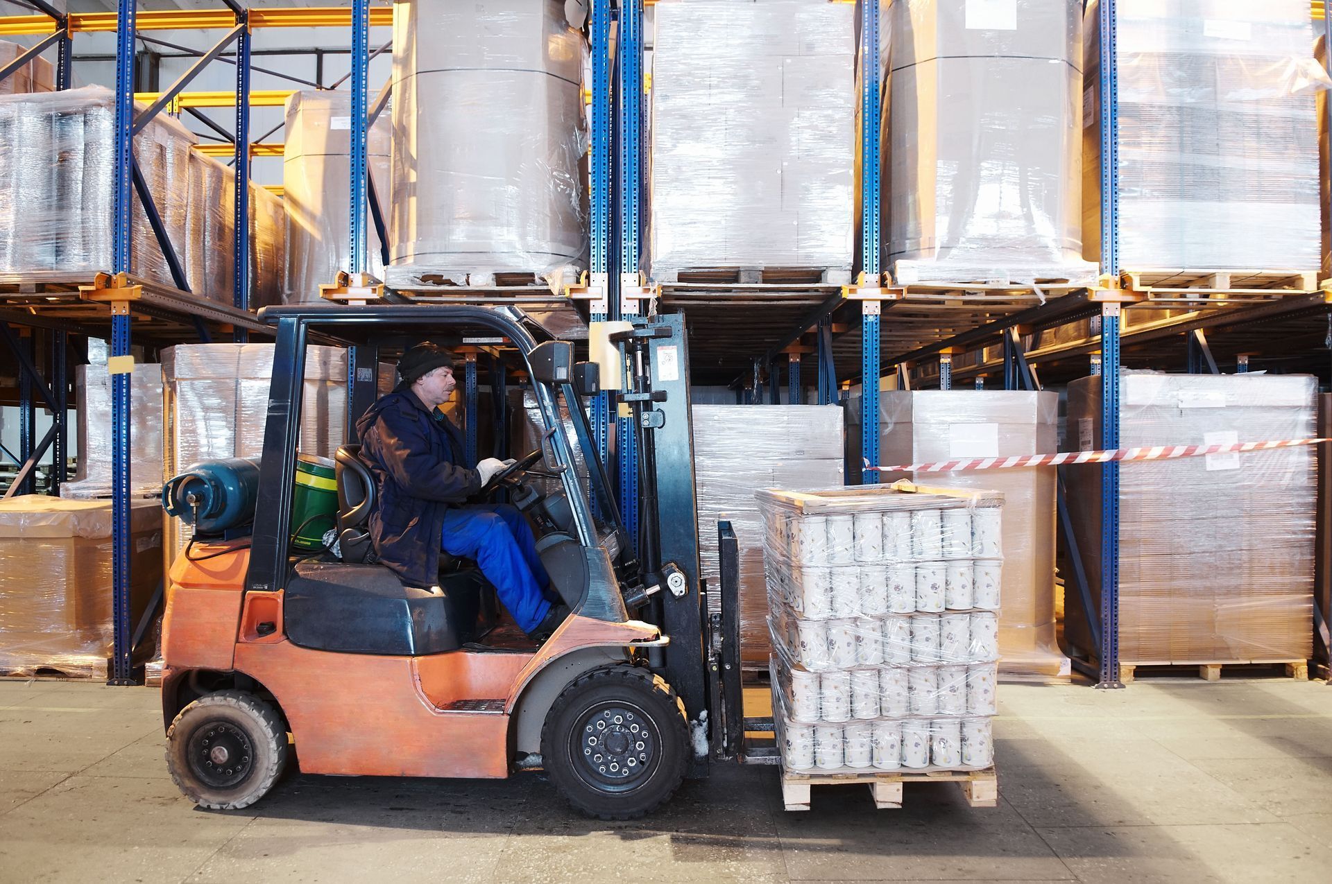 Forklift in warehouse transporting a pallet of canned goods.