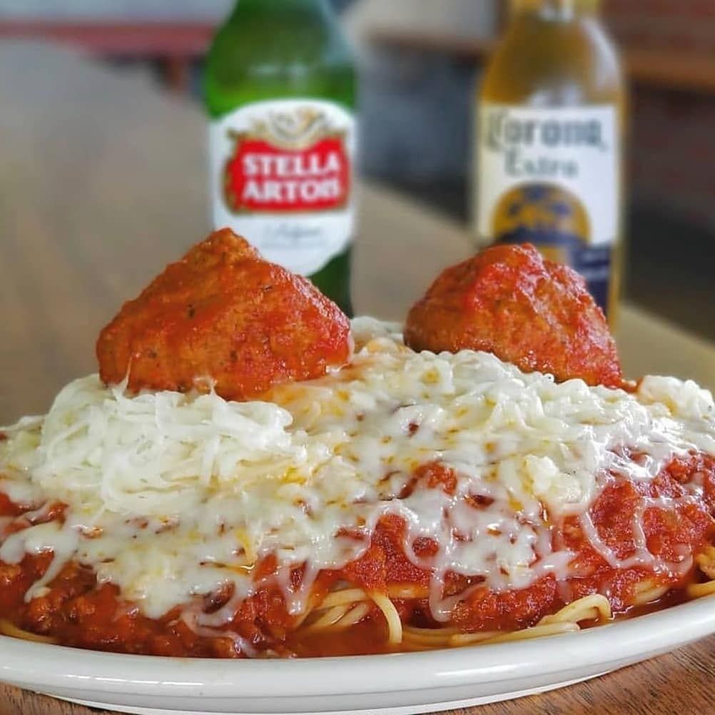 A plate of spaghetti and meatballs with a bottle of stella artois in the background