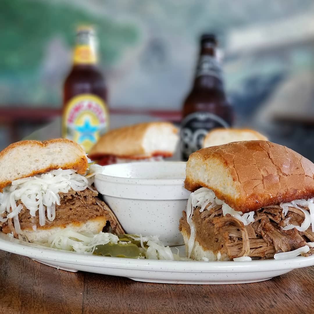 Two pulled pork sandwiches on a plate with a bowl of dipping sauce.