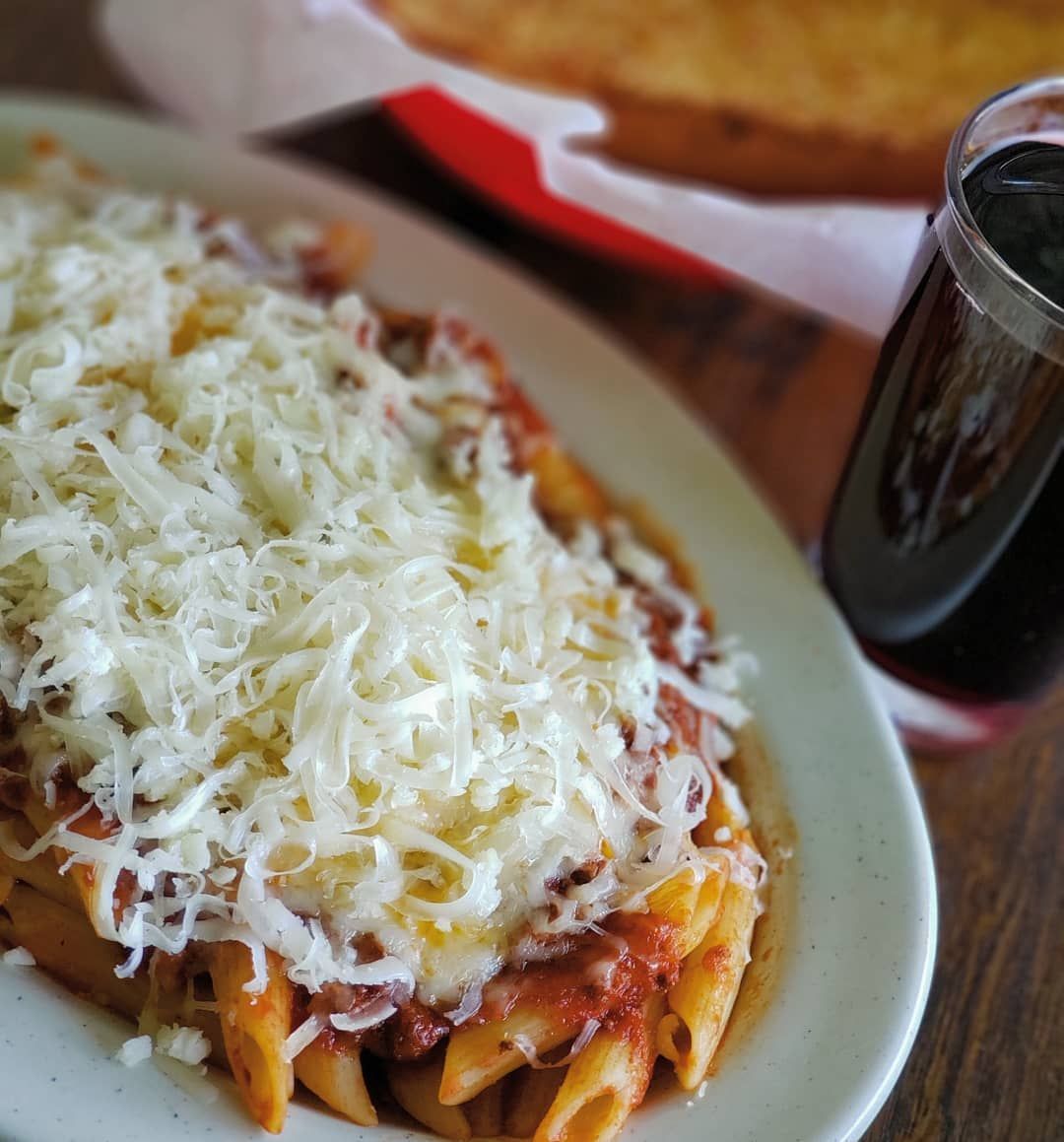 A plate of pasta with sauce and cheese next to a glass of soda