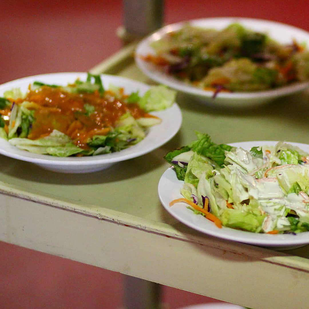 Three plates of salad are on a tray on a table.