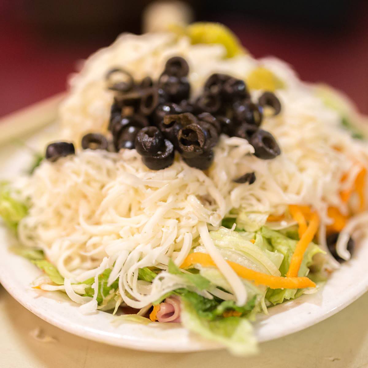 A white plate topped with noodles , olives and other vegetables.