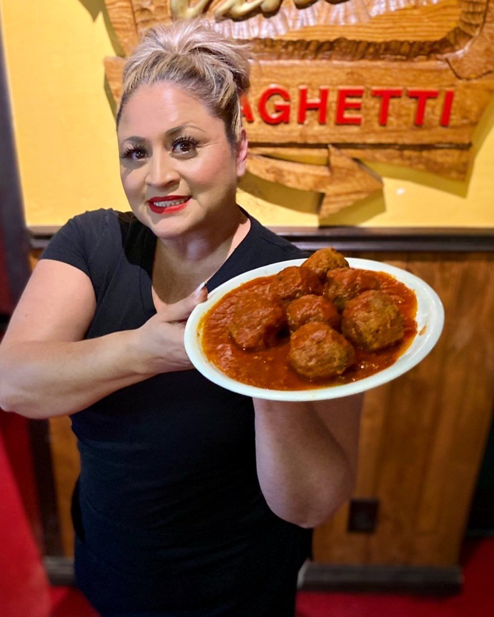 A woman is holding a plate of meatballs in front of a sign that says spaghetti