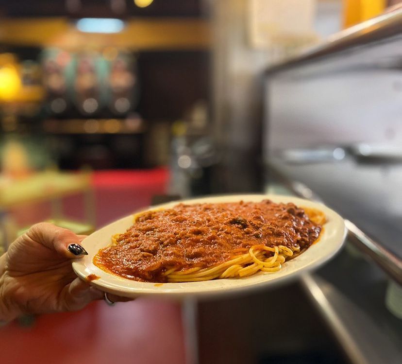 A person is holding a plate of spaghetti with meat sauce.