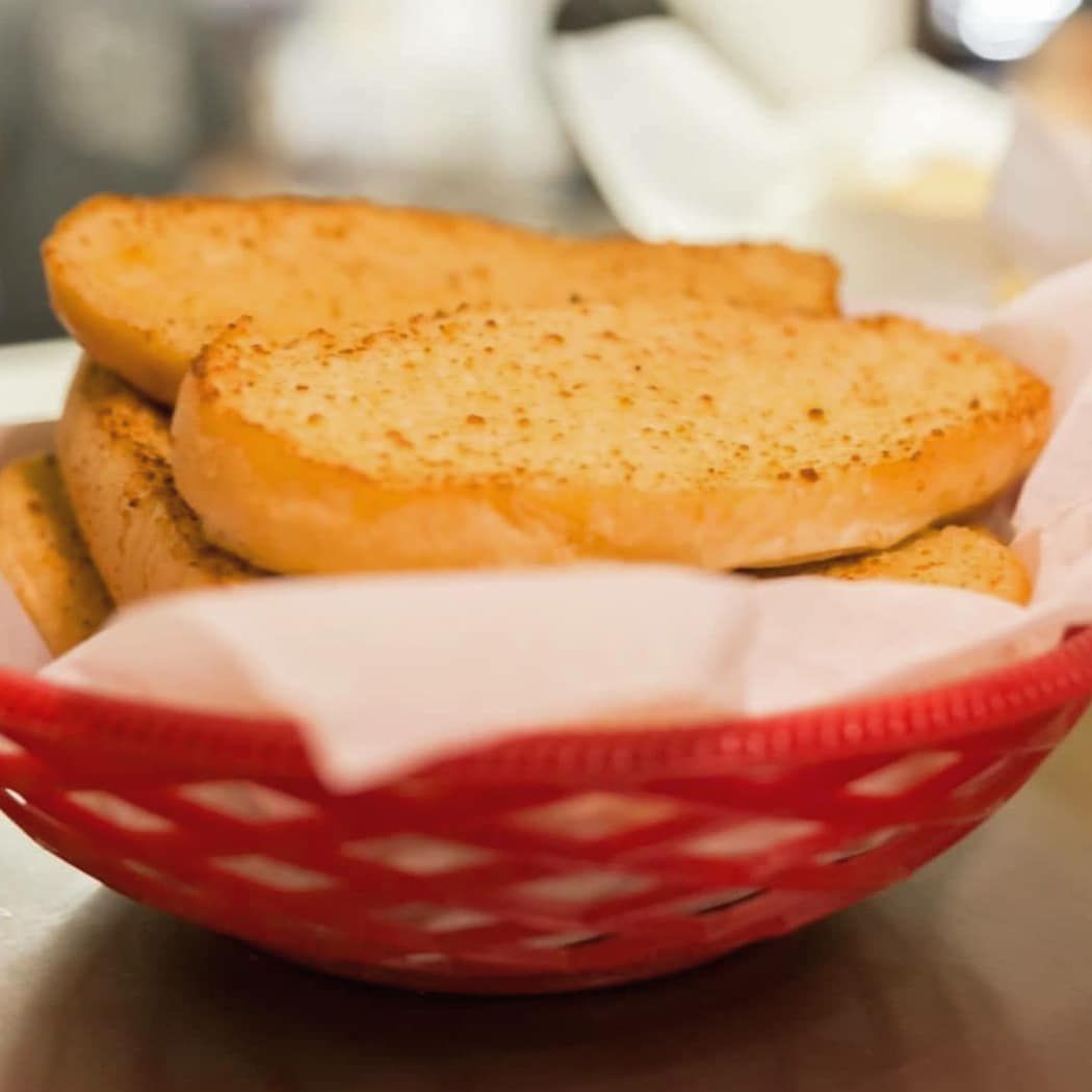Garlic bread is in a red basket on a table.