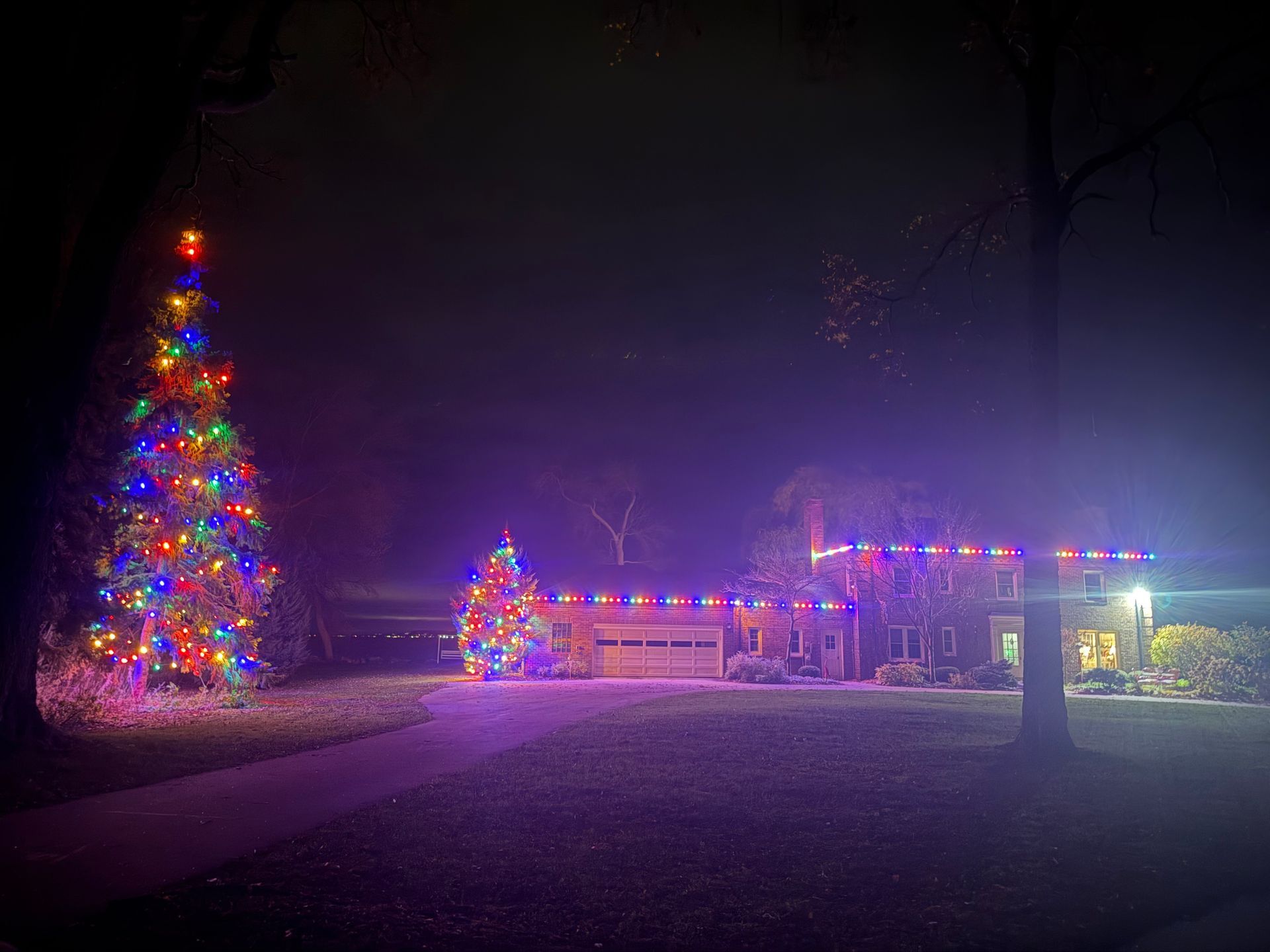 A christmas tree is lit up in front of a house at night.
