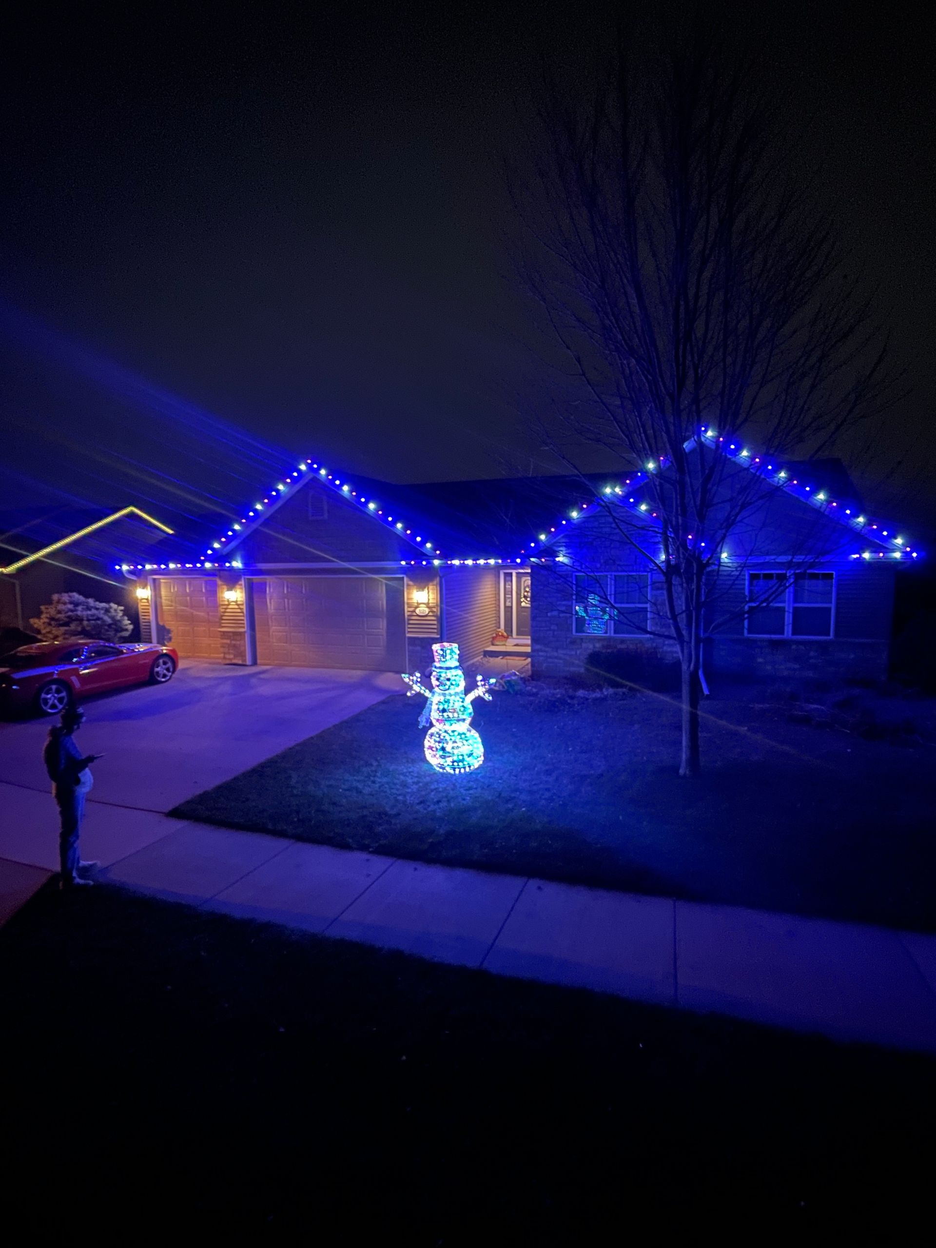A snowman is lit up in front of a house with blue lights.