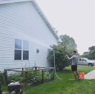 A man is cleaning the side of a house with a pressure washer.