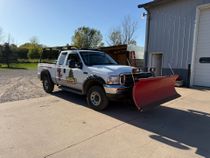 A yellow snow plow is plowing snow in a parking lot