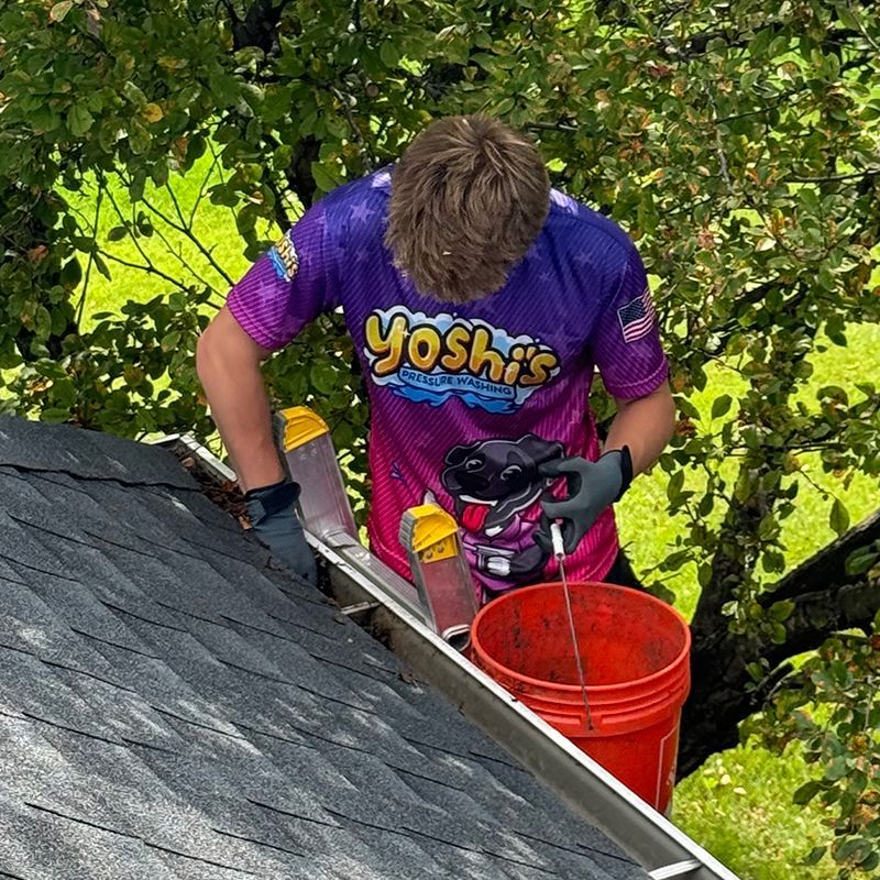 A man in a purple shirt is cleaning gutters on a roof