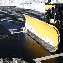 A yellow snow plow is plowing snow in a parking lot