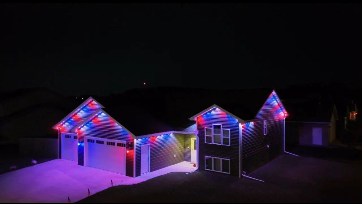 House decorated with red, white, and blue lights. Lit up at night, the house is visible from the dark sky.