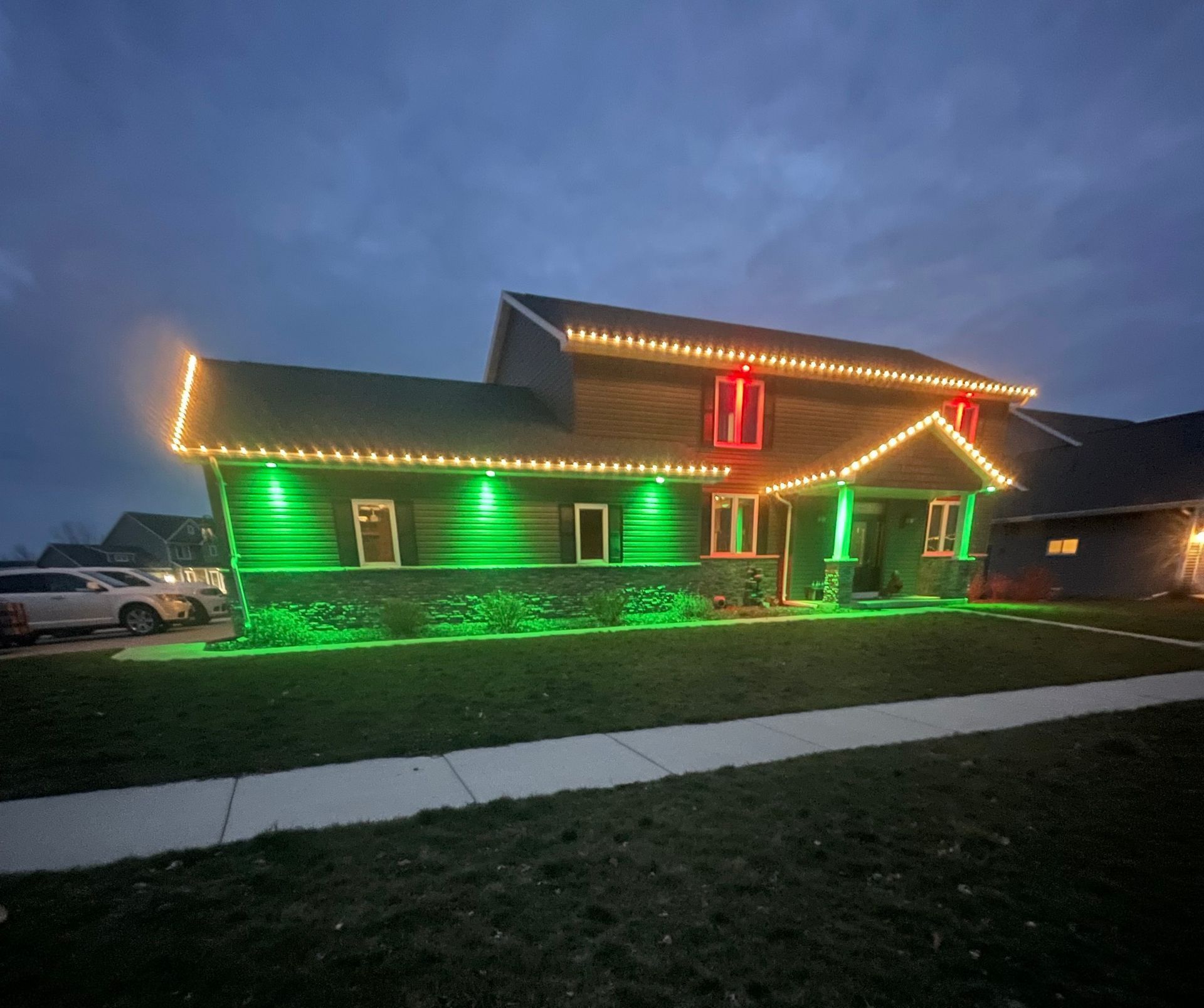 House decorated with green and red Christmas lights at dusk.