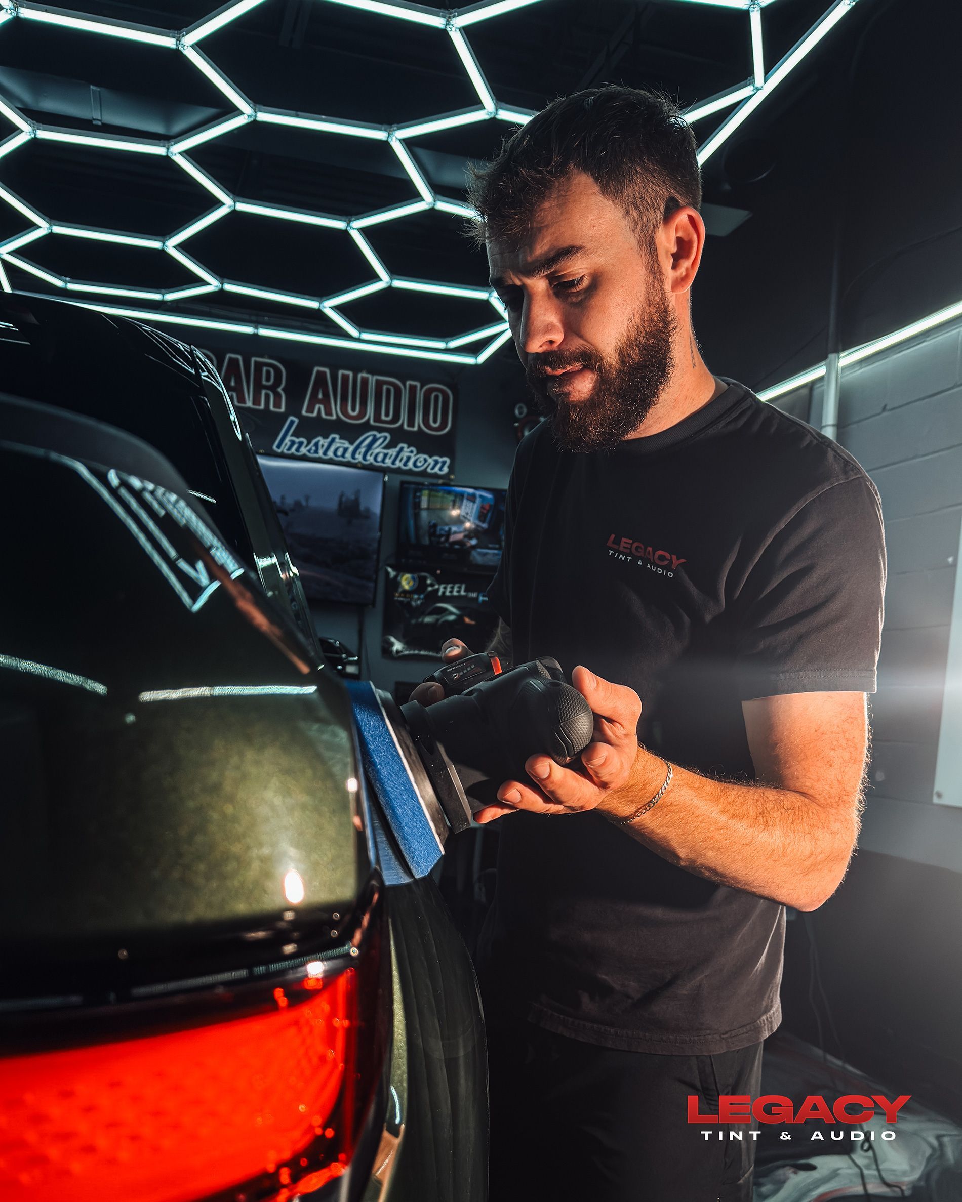 Man detailing a black car under bright geometric LED lights in a studio setting